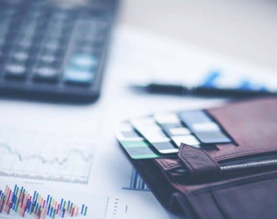 A wallet with credit cards on a table with papers featuring charts and graphs, and a computer keyboard, representing conjoint analysis.