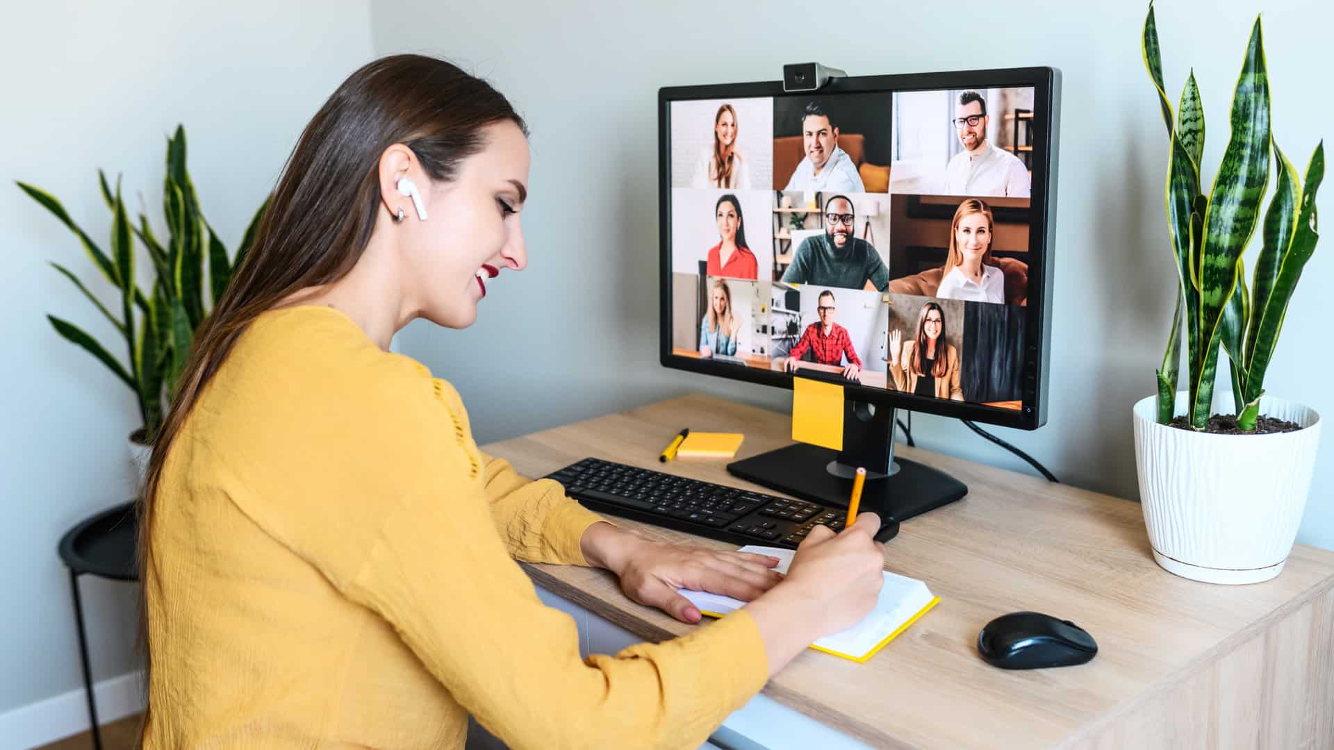 Virtual conference, morning meeting online. A young woman is using app on pc for connection with colleagues, employees, she is writing in notebook. Video call with many multiracial people togethe