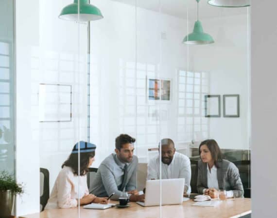 A diverse group of data scientists practicing communication skills around a laptop in an office.