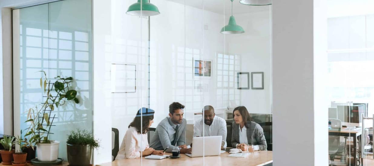 A diverse group of data scientists practicing communication skills around a laptop in an office.